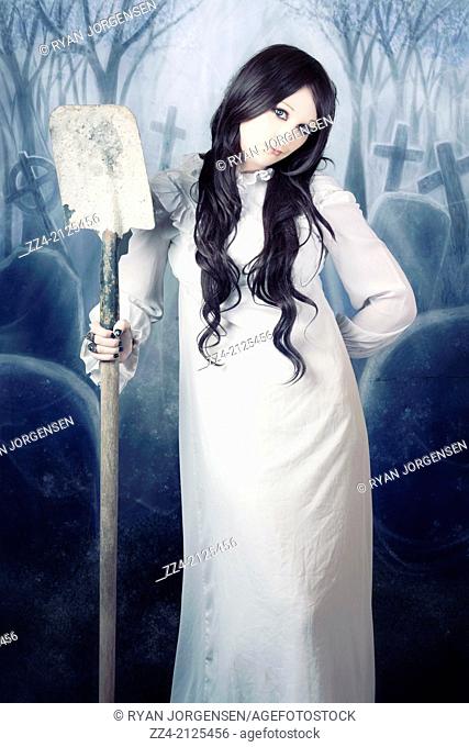 Mysterious woman in long white dress standing in a misty cemetery at the dead of night with shovel in hand, digging up graves and resurrecting the dead