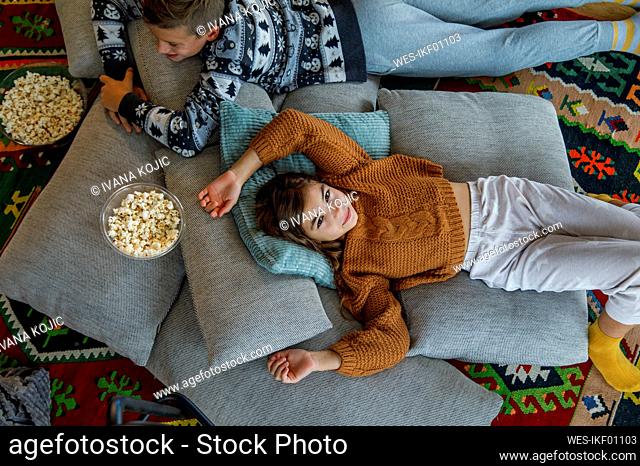 Girl resting on pillows by brother in living room