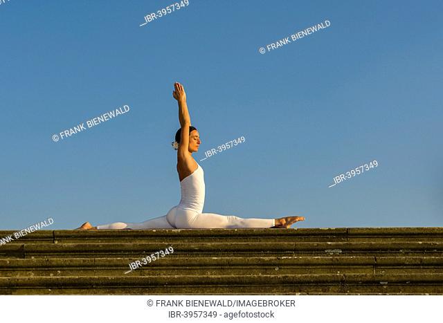 Young woman practising Hatha yoga, outdoors, showing the pose Anjaneyasana, Hanumanasana, Split