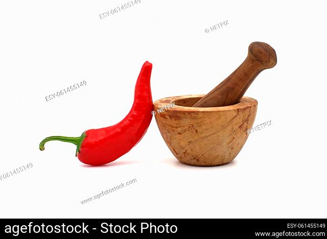 Old rustic wooden pestle and mortar alongside an fresh red chili pepper isolated on a white background