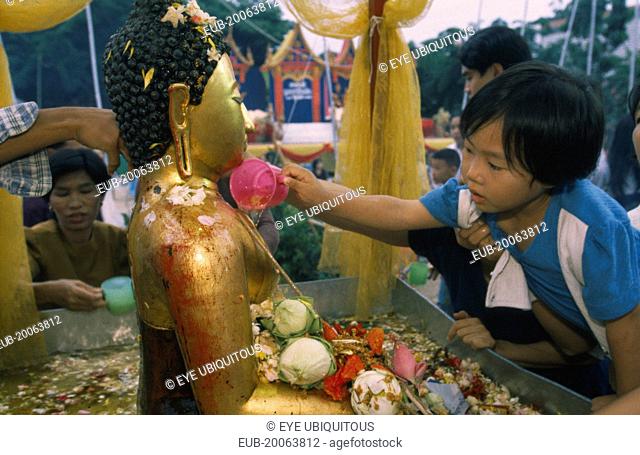 Inthakhin Ceremony. Young boy bathing Phra Fon Saen Ha Buddha statue surrounded by floral offerings and pool