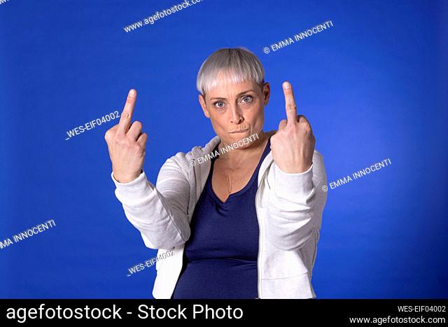 Angry woman showing obscene gesture against blue background