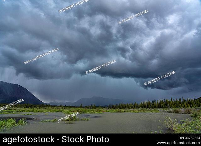 A storm creates drama in the Yukon skies during a warm summer day. Heavy rain and hail can be seen; Whitehorse, Yukon, Canada