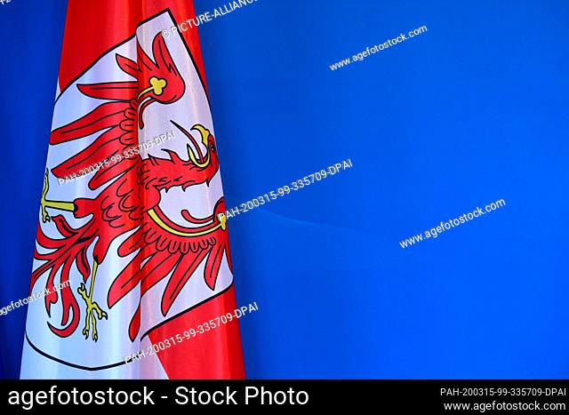 13 March 2020, Brandenburg, Potsdam: The flag with the logo of the stylized eagle in front of the blue wall of the press conference room in the State...