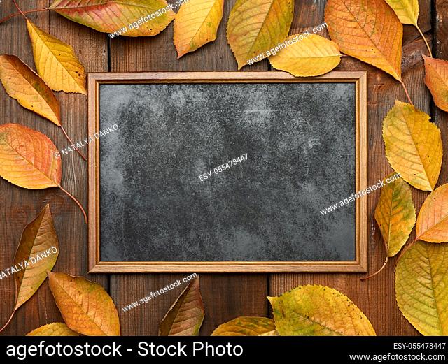 empty wooden chalk board on a brown wooden background and yellow cherry leaves, place for an inscription