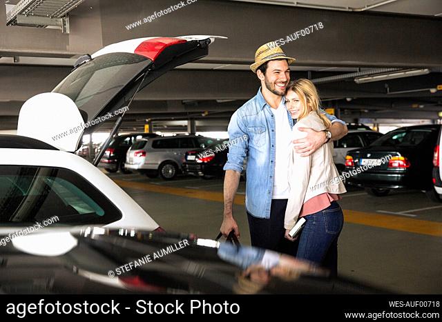 Smiling man embracing girlfriend in airport parking lot