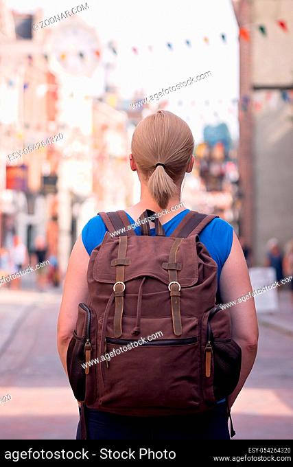 Blond Caucasian female standing on a high street in an English town carrying small brown retro backpack