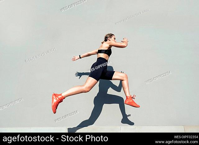Young athlete jumping by gray wall on sunny day