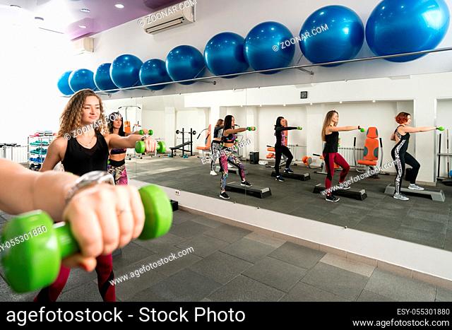 Group of girls in sportswear shot in a gym exercising on step platforms with dumbells