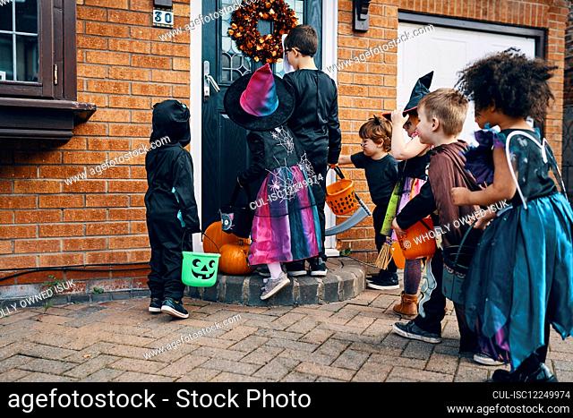 A group of children dressed up for Halloween at a front door with buckets trick or treating