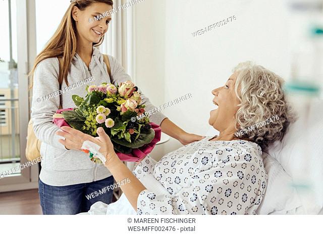 Granddaughter visiting grandmother in hospital, bringing bunch of flowers