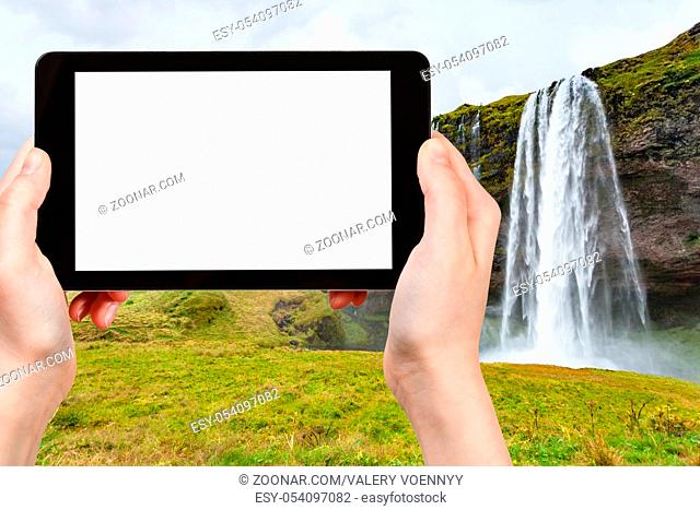 travel concept - tourist photographs Seljalandsfoss waterfall of Seljalands River in Katla Geopark on Icelandic Atlantic South Coast in autumn on tablet with...