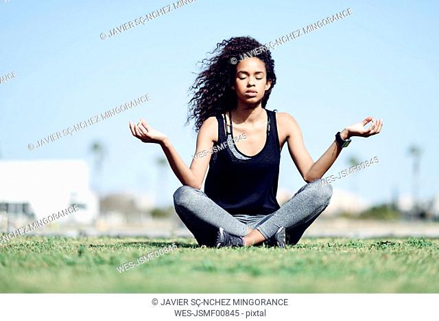 Sporty young woman doing yoga on lawn