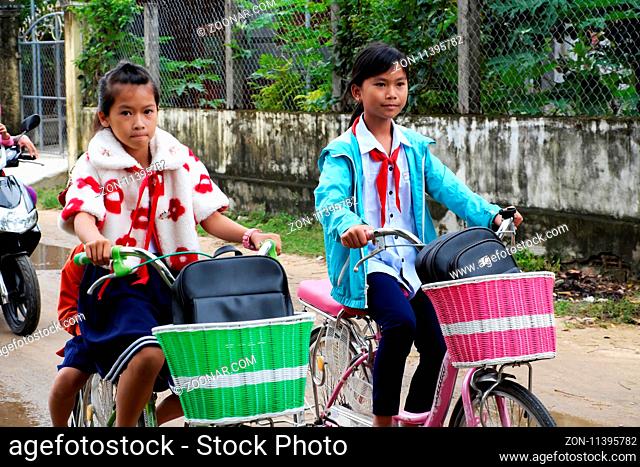 BINH DINH, VIET NAM- NOV 3, 2017:Group of Vietnamese children coming home from school by bicycle, crowd Asian little girl ride cycle on country road, Vietnam