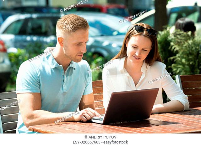Young Couple Sitting On Bench Using Laptop