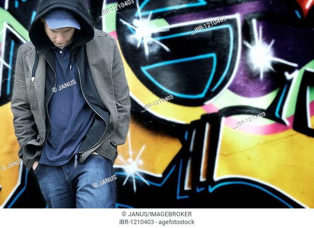 Portrait of a young man wearing a cap, wearing a hoodie jacket, in front of a graffiti-sprayed wall