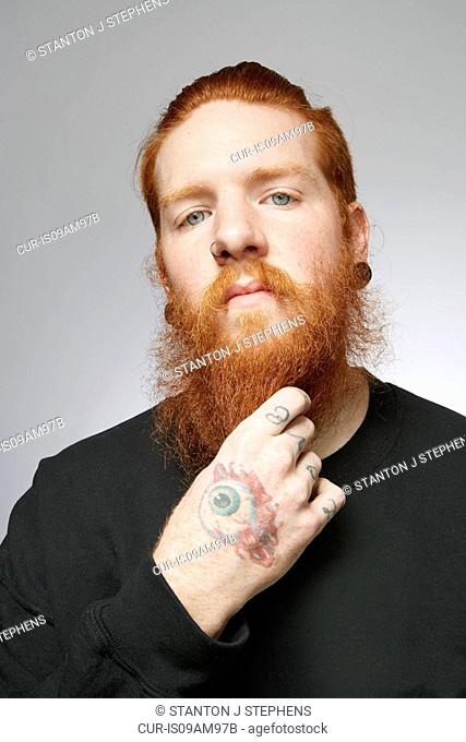 Studio portrait of young man with red hair stroking beard