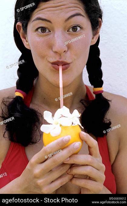 Young woman drinking cocktail through straw out of orange
