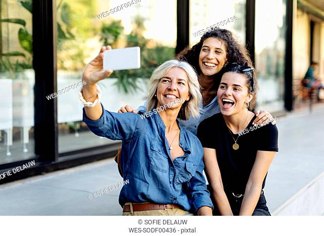 Three laughing women taking selfie in the city