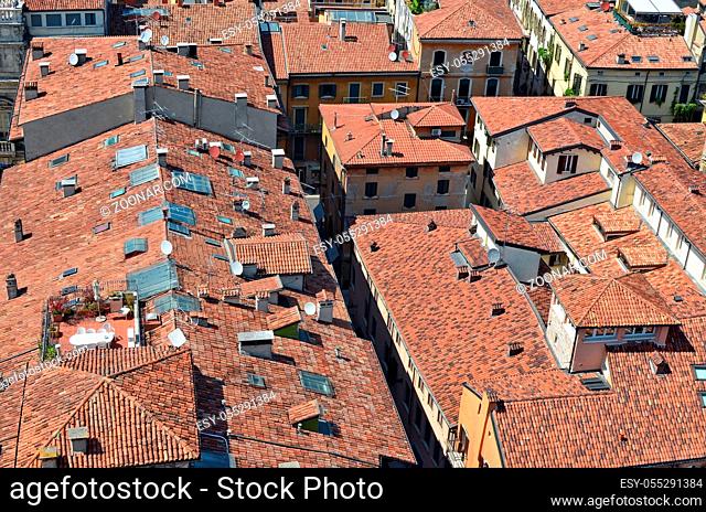 On the red tiled roofs of a small no name Italian city there are many satellite TV antennas and roof windows. Bird's eye view summer sunny day landscape