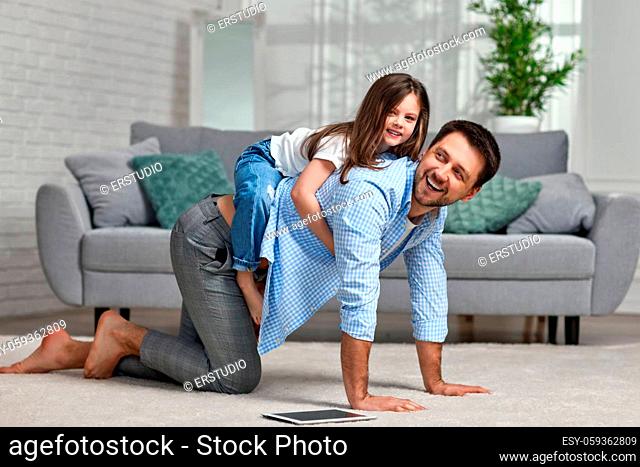 Happy dad carrying child on back, father playing with cute little daughter at home, piggy back