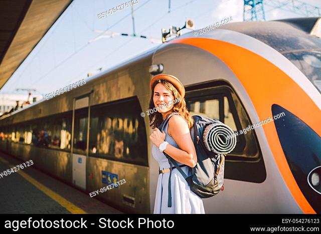 theme railway and travel. Portrait young caucasian woman with toothy smile standing at train station train background with backpack and equipment for tourism...