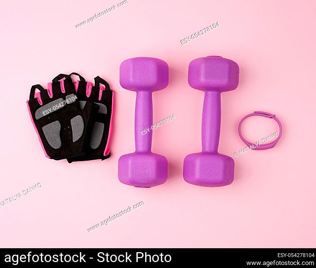 pair of purple plastic dumbbells and black gloves on a pink background, training equipment, top view