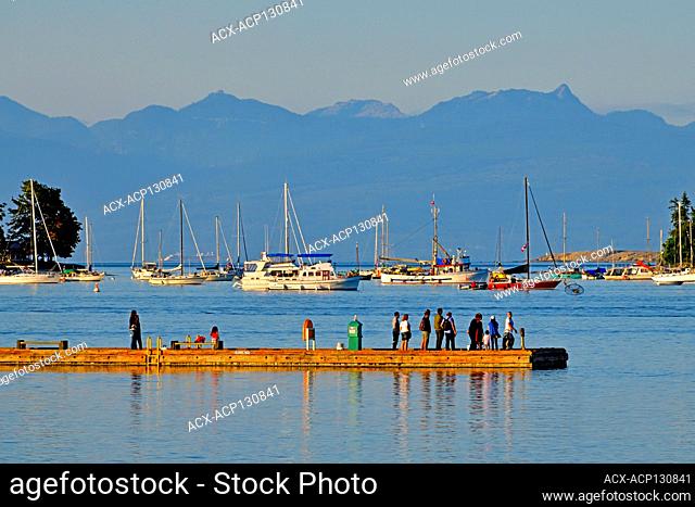 A landscape image of the fishing pier with people fishing and sight seeing with evening light in the harbour at Nanaimo on Vancouver Island British Columbia...