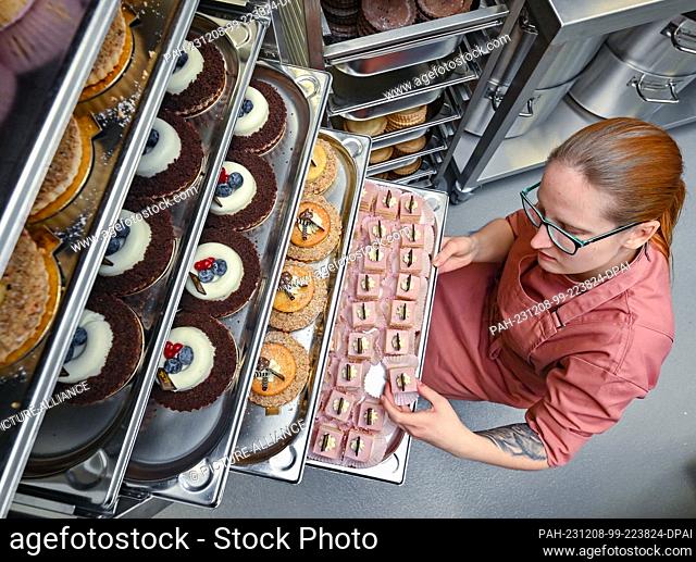 08 December 2023, Brandenburg, Fürstenwalde: Michelle Thiede, pastry chef, places small handmade cakes on a tray at the opening of the Le Gateau rose cake...