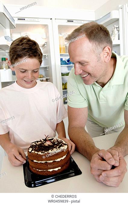 Close-up of a boy and his father standing in front of a cake