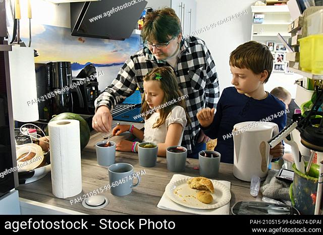 14 May 2021, Saxony, Leipzig: Ronny Steglich prepares tea with the children Timon (r, 11) and Kiana (l, 7) in the eat-in kitchen of their new 5-room apartment