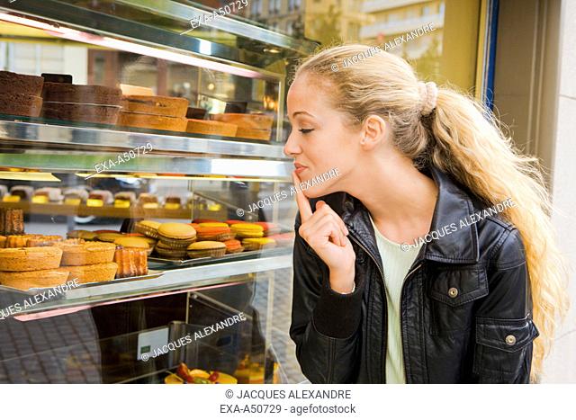 Young woman shopping and looking through the display window of a bakery