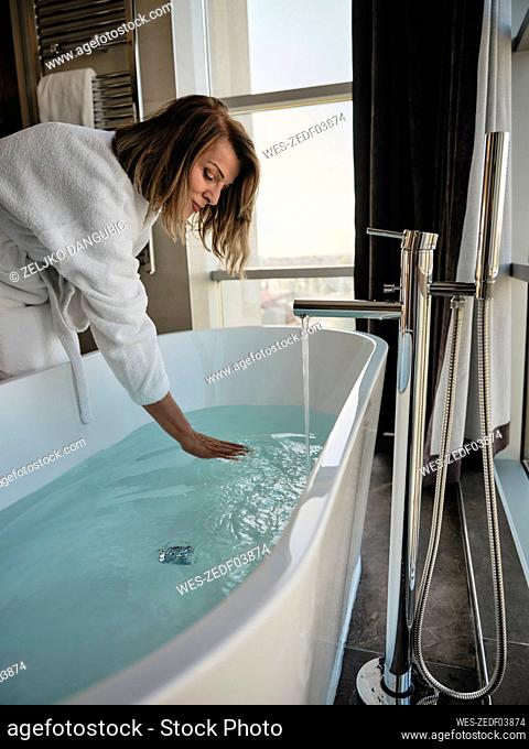 Senior woman bending over while examining temperature in bathtub at luxury hotel