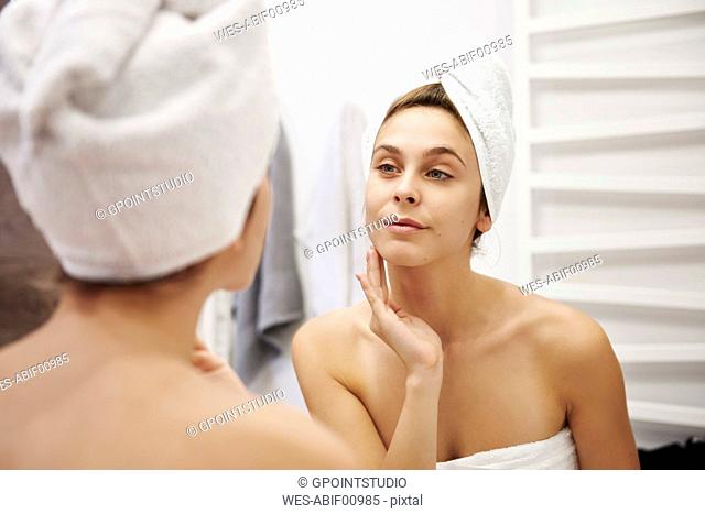 Mirror image of young woman examining her face in the bathroom