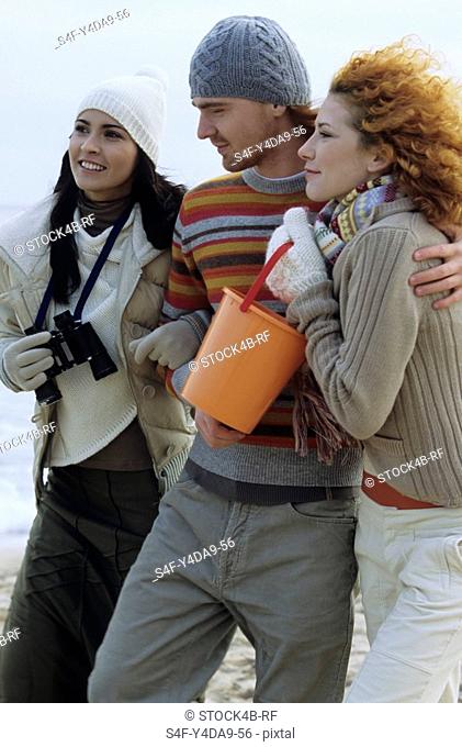 Two young Women with a Man between them strolling along the Beach - Friendship - Trip - Season