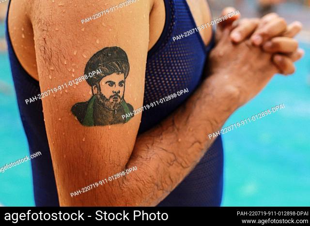 19 July 2022, Iraq, Baghdad: An Iraqi man is seen with a portrait of Iraqi Shia cleric Muqtada al-Sadr..tattooed on his arm, at an Aqua Park in Baghdad