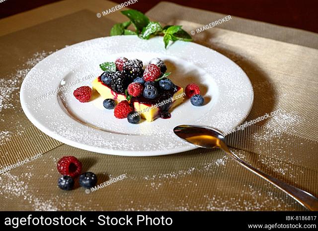 A slice of cheesecake with fresh raspberries and blackberries and a layer of icing sugar on a white plate