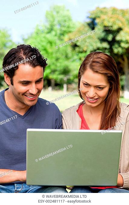 Two friends smiling happily as they watch something on a tablet in a bright park