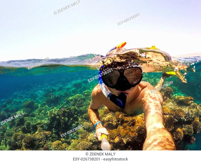 Underwater and surface split view in the tropics paradise with snorkeling man, fish and coral reef, under and above waterline, beautiful view on tropical sea