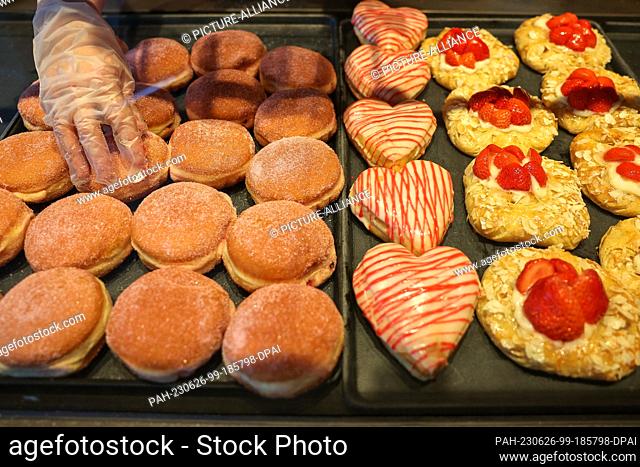 26 June 2023, Saxony, Leipzig: An employee is putting pancakes (Berliner or Krapfen) into the display at a bakery. On the same day