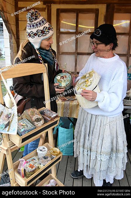 16 December 2023, Saxony, Schkeuditz: A visitor looks at handmade caskets by Kerstin Stadler (r) from the Biedermeier period at the Victorian Christmas market...