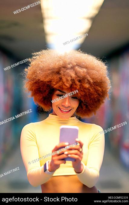 Smiling woman with redhead Afro hairstyle using smart phone