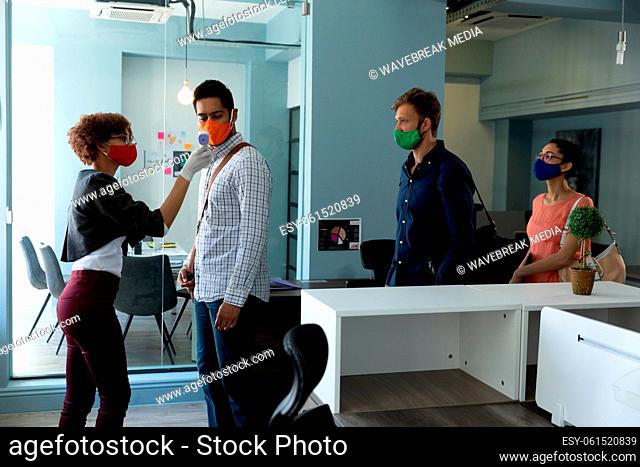 Mixed race woman wearing face mask checking temperature of colleagues