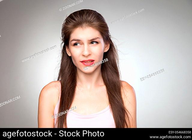Messed up girl feel her fault and biting her lips. Studio portrait on grey vignette background