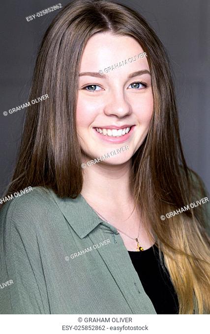 Headshot of a beautiful young woman taken in a studio on a grey background. She is wearing casual clothing and looking at the camera and smiling