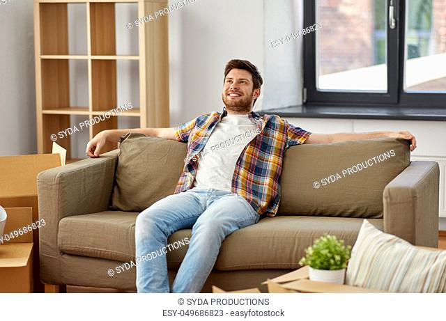 happy man with boxes sitting on sofa at new home