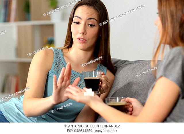 Guest rejecting sugar into coffee cup sitting on a couch in the living room at home