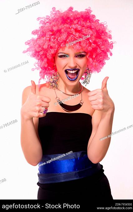 Portrait of beautiful party girl in pink wig smiling and giving thumb-ups. Happy lady in party costume looking very excited isolated on white