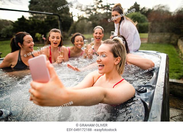 Small group of female friends enjoying a weekend away. They are taking a group selfie while sitting in a hot tub