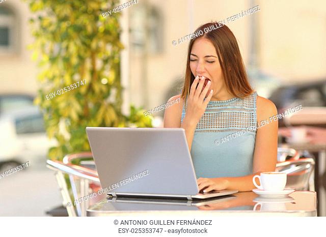 Tired woman yawning and working with a laptop in a restaurant during breakfast